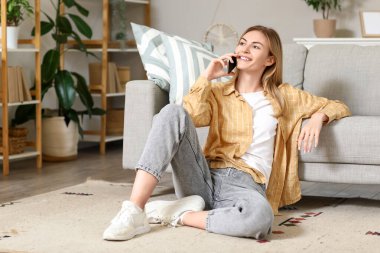 Evde cep telefonuyla konuşan genç bir kadın.