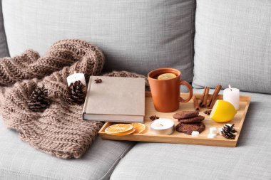 Limonlu çay tepsisi, kurabiyeler, yanan mumlar ve koltukta kitap.