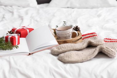 Kakaolu kitap, sıcak çoraplar ve Noel hediyeleri yatakta, yakın plan.