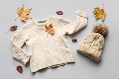 Sıcak çocuk süveteri, şapkası ve gri arka planda düşmüş yaprakları olan kompozisyon