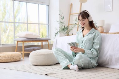 Kulaklıkları ve banknotları olan genç bir kadın yatak odasında oturuyor.