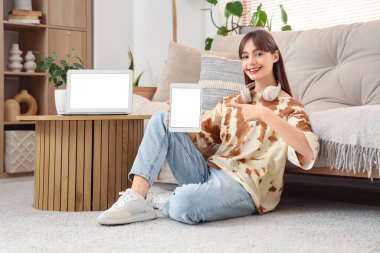 Boş tablet bilgisayarı ve dizüstü bilgisayarı olan genç bir kadın evde oturuyor.