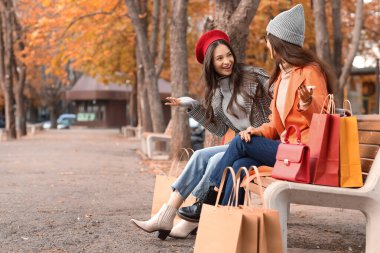 Alışveriş torbalı bayan arkadaşlar sonbahar günü parkta oturuyorlar.