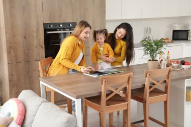 Genç lezbiyen çift mutfakta kızlarına kitap okuyor.