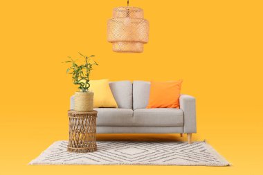 Sarı arka planda bambu saplı masa, kanepe, halı ve lamba.