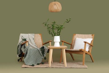 Vazoda bambu saplı masa, yeşil arka planda koltuklar ve lamba.