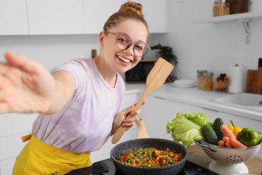 Kızarmış sebzeli genç bir kadın mutfakta selfie çekiyor.