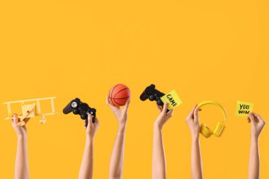 Oyun pedleri, oyuncakları, kulaklıkları ve sarı arka planda yapışkan kağıtları olan kadın elleri.