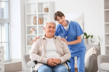 Kadın doktor evde tekerlekli sandalyedeki olgun adama sarılıyor.