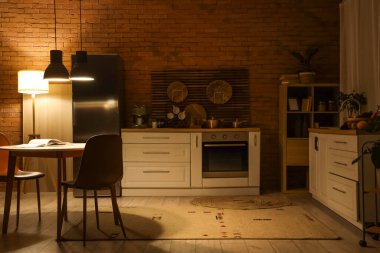 Karanlık mutfağın içinde tezgahlar, yemek masası ve geceleri parlayan lambalar var.