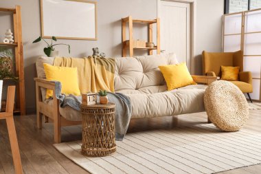 Aydınlık oturma odasının içinde bej kanepe, masa ve bitkiler var.