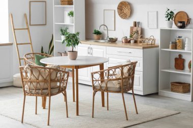 Beyaz tezgahları, yemek masası ve bitkileri olan aydınlık mutfağın içi.