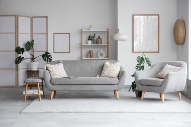 Gri kanepeli, koltuklu ve yumuşak banklı aydınlık oturma odasının içi.