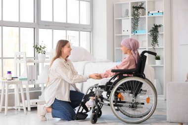 Annesi hastanede el ele tutuşurken tekerlekli sandalyedeki kemoterapiden sonra küçük bir kız. Çocukluk kanseri farkındalığı