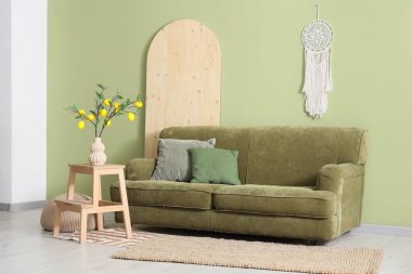 İçinde yeşil kanepe, ağaç dalları ve vazoda limonlar olan oturma odasının içi.