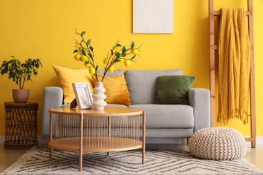 Oturma odasının içinde kanepe, ağaç dalları ve vazoda limonlar var.