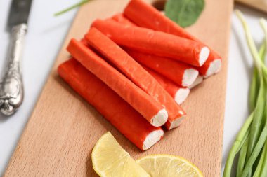 Lezzetli yengeç çubuklu ahşap tahta, gri arka planda limon dilimleri ve yeşil soğan, yakın plan.