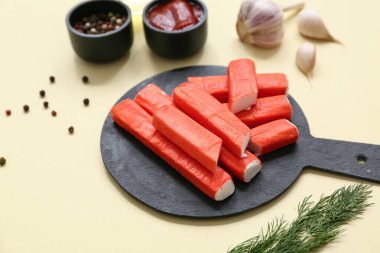 Lezzetli yengeç çubukları ve sarı arka planda farklı baharatlar olan siyah tahta.