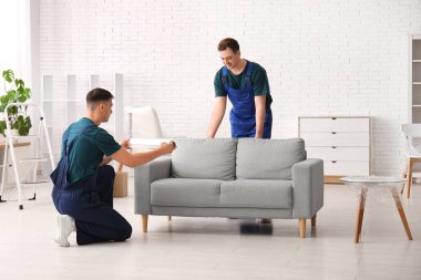 Erkek yükleyiciler kanepeyi streç filmle dolduruyor.