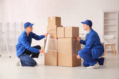 Erkek işçiler karton kutuları gerilmiş filmlerle dolduruyorlar.