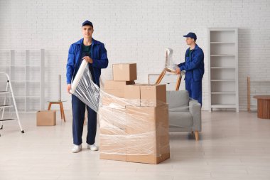 Erkek işçi, odada streç filmle karton kutuları paketliyor.