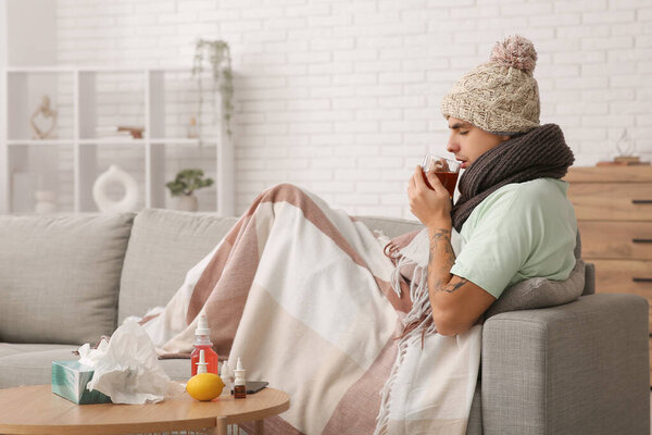Нездоровый молодой человек пьет чай на диване дома