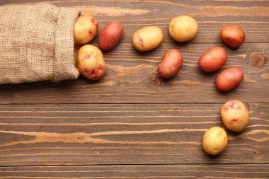 Tahta arka planda taze çiğ patatesli çuval.