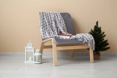 Sıcak battaniyeli rahat koltuk, küçük Noel ağacı ve bej duvarın yanındaki fenerler.