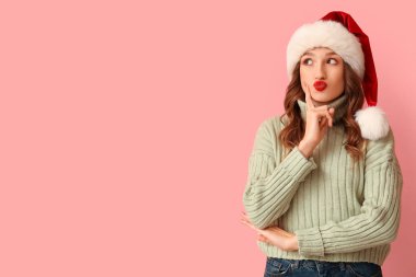 Pembe arka planda Noel Baba şapkalı düşünceli genç kadın.