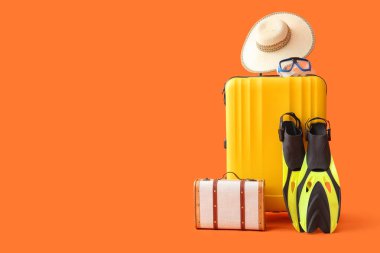 Paletli bavullar ve turuncu arka planda plaj aksesuarları.