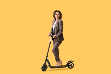 Turuncu arka planda elektrikli scooter kullanan olgun bir iş kadını.