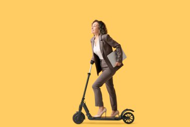 Olgun iş kadını scooter sürüyor ve turuncu arka planda klasörü tutuyor.