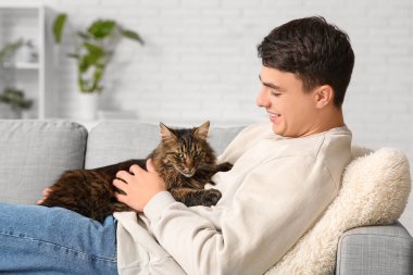 Evdeki kanepede tatlı kedili genç bir adam yatıyor.