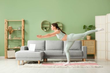 Güzel genç bir kadın oturma odasında yoga yapıyor.