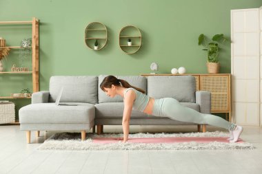 Güzel genç bir kadın oturma odasında yoga yapıyor.