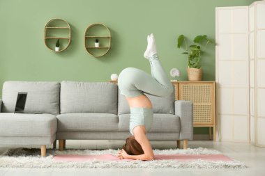 Güzel genç bir kadın oturma odasında yoga yapıyor.