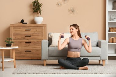 Oturma odasında dambıllarla antrenman yapan güzel bir genç kadın.