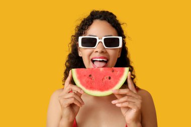 Sarı arka planda taze karpuz ve mayo giymiş mutlu Afro-Amerikan kadın.