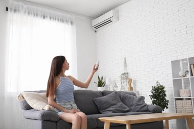 Evdeki kanepede oturan klimalı uzaktan kumandalı güzel bir genç kadın.
