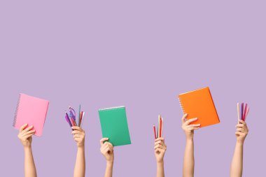 Leylak arka planında farklı okul malzemelerine sahip kadın eller.