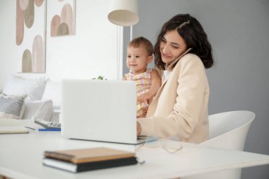 Çalışan anne evde bebeğiyle cep telefonuyla konuşuyor.