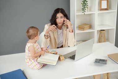 Evde cep telefonuyla konuşan küçük bebeğiyle çalışan bir anne.