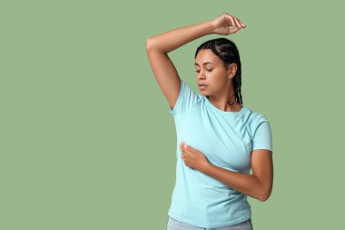 Genç Afro-Amerikalı bir kadın yeşil arka planda göğüslerini kontrol ediyor. Kanser farkındalığı kavramı