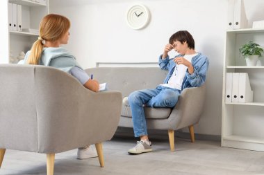 Üzgün genç çocuk ofiste psikologla konuşuyor.