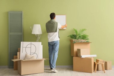 Evdeki yeşil duvara boş bir çerçeve asan genç adam.