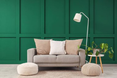 Koltuk, çiçekli kahve masası, lamba ve puf yeşil duvarın yanında.