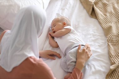 Başörtüsü içinde Müslüman bir anne ve evde yatağında uyuyan şirin bir bebek.