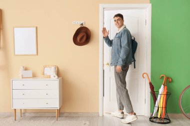 Sırt çantalı genç adam koridorda el sallıyor.