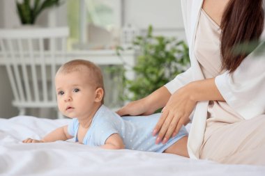 Güzel, genç Asyalı bir anne ve tatlı küçük bebeği evde, yatakta oturuyor, yakın plan.