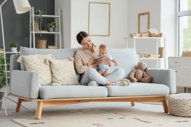 Güzel, genç, mutlu bir Asyalı anne ve tatlı bebeği evdeki kanepede oturuyor.